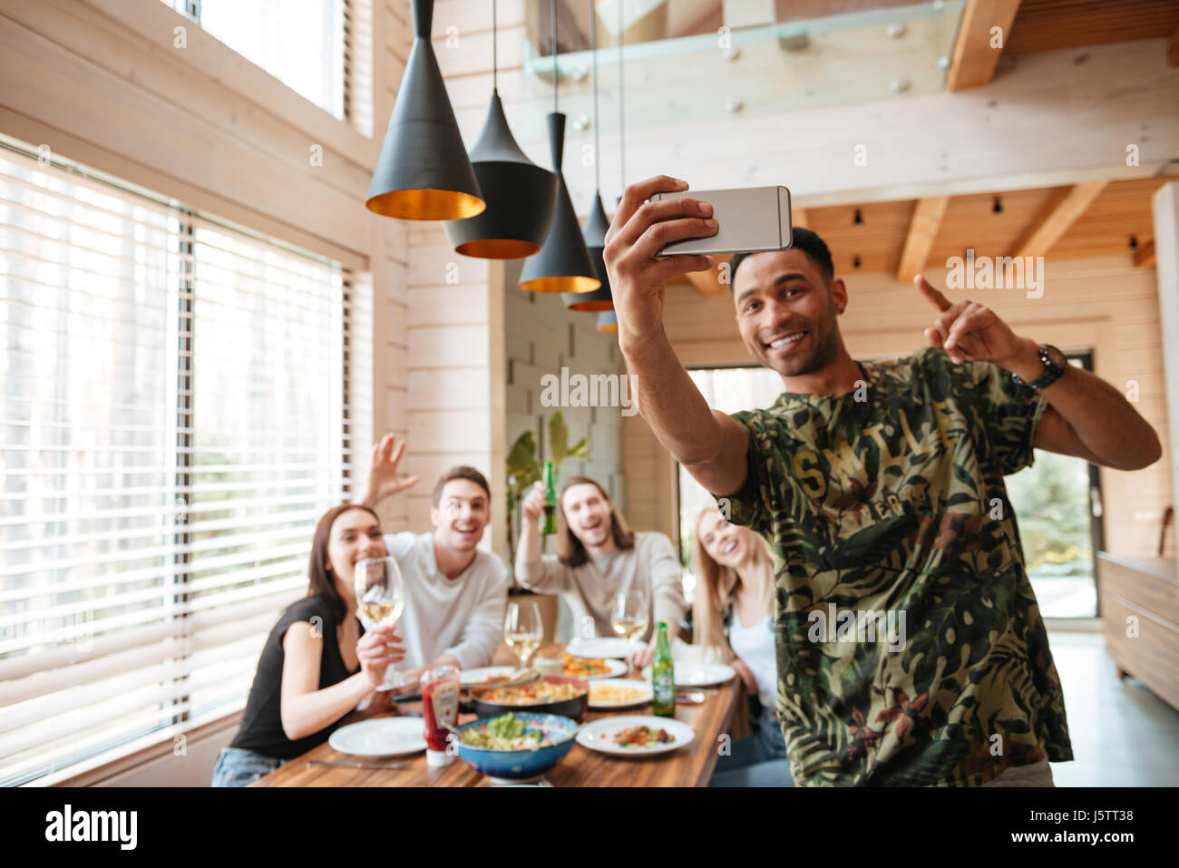 Cheerful african young man taking selfie with his friends at the table ...