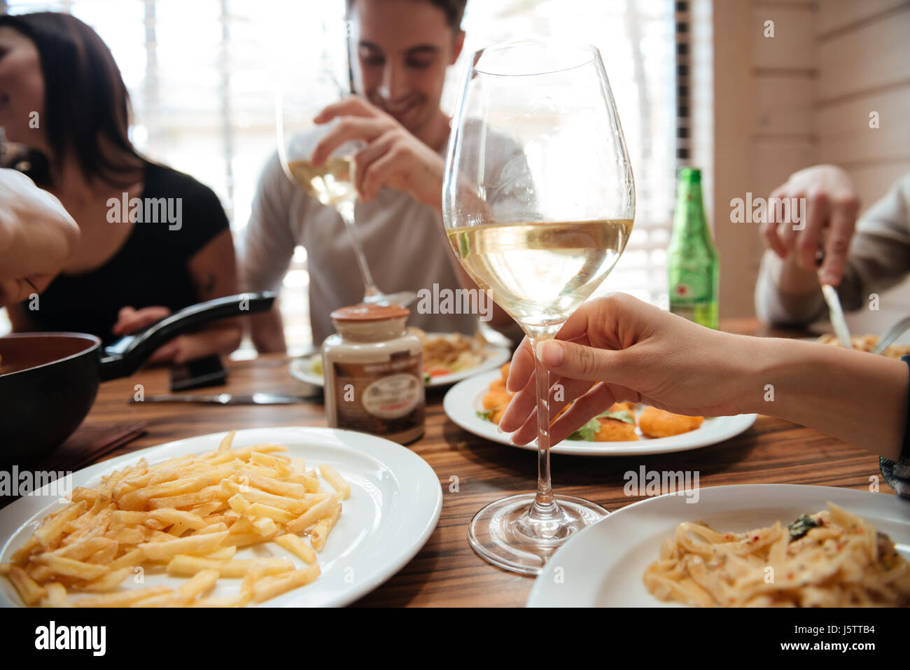 Closeup of group of people drinking wine and eating pasta at the table ...