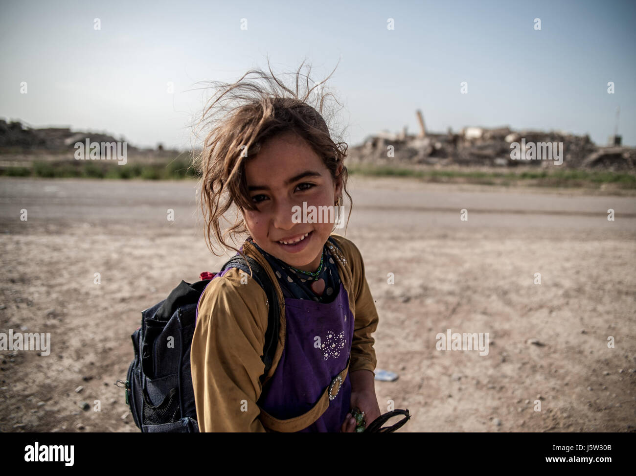 An internally displaced girl stands outside Hammam al Alil camp  near buildings ruined by Islamic State Stock Photo