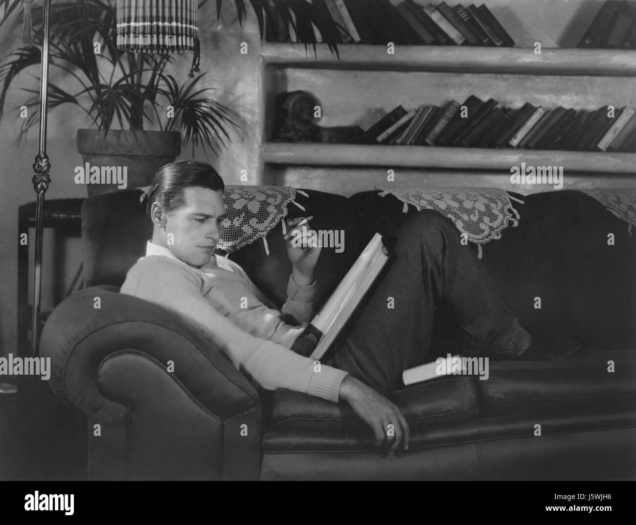 Actor Richard Arlen, Publicity Portrait Smoking Cigarette and Reading Script on Sofa, 1930's Stock Photo