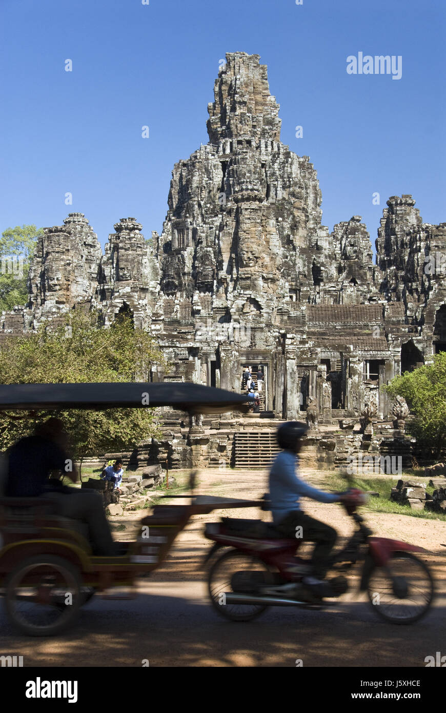 Motorcycles pass by the Bayon, a Buddhist temple decorated with massive stone faces, Siem Reap, Cambodia. Stock Photo