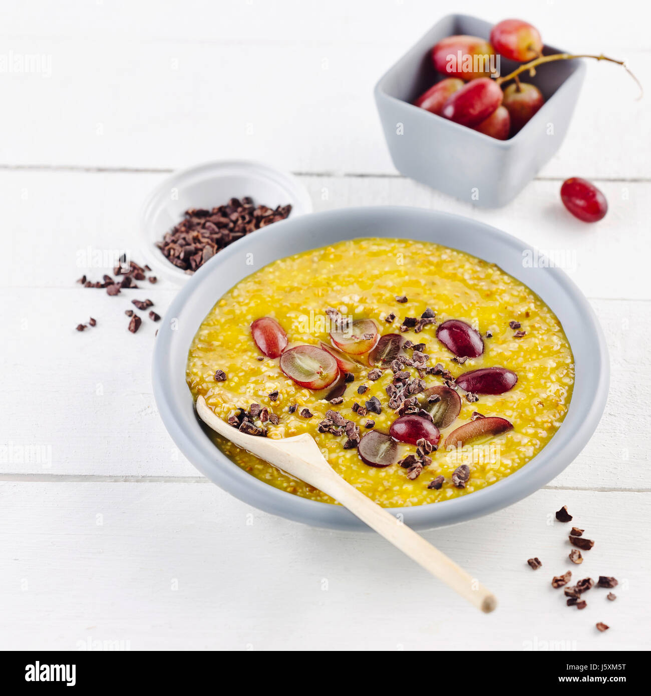 Orange grain porridge with grapes and cocoa nibs Stock Photo