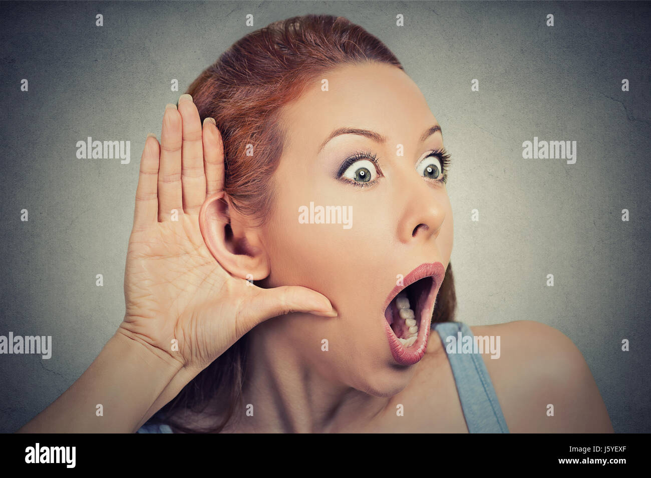 Closeup portrait surprised young nosy woman hand to ear gesture carefully intently secretly listening juicy gossip conversation news privacy violation Stock Photo