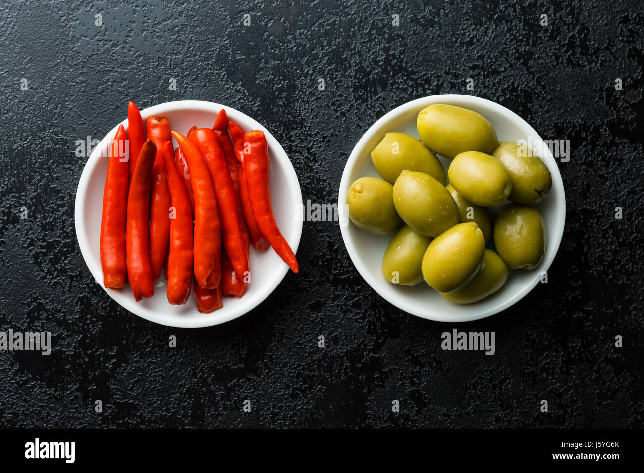 Pickled chili peppers and green olives in bowl. Top view Stock Photo