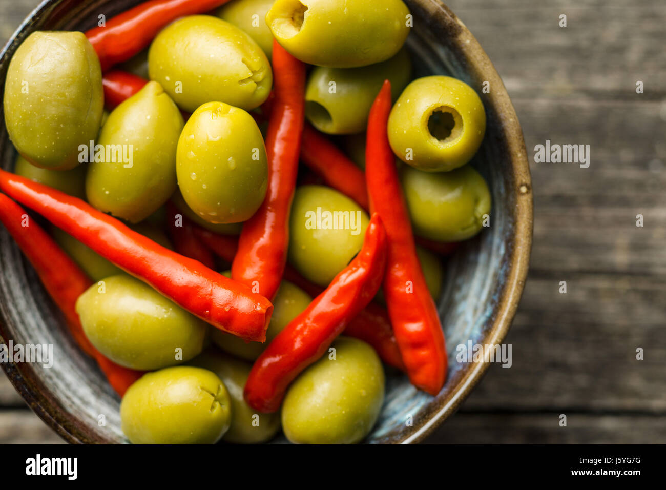 Pickled chili peppers and green olives in bowl. Top view Stock Photo