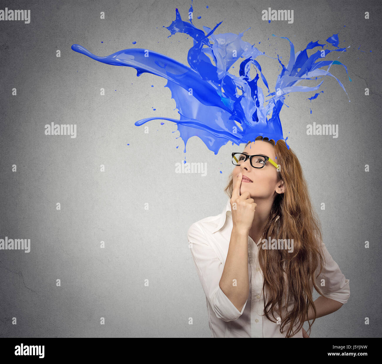Thoughtful businesswoman looking up with colorful splashes coming out of her head isolated on gray wall background. Face expression perception Stock Photo