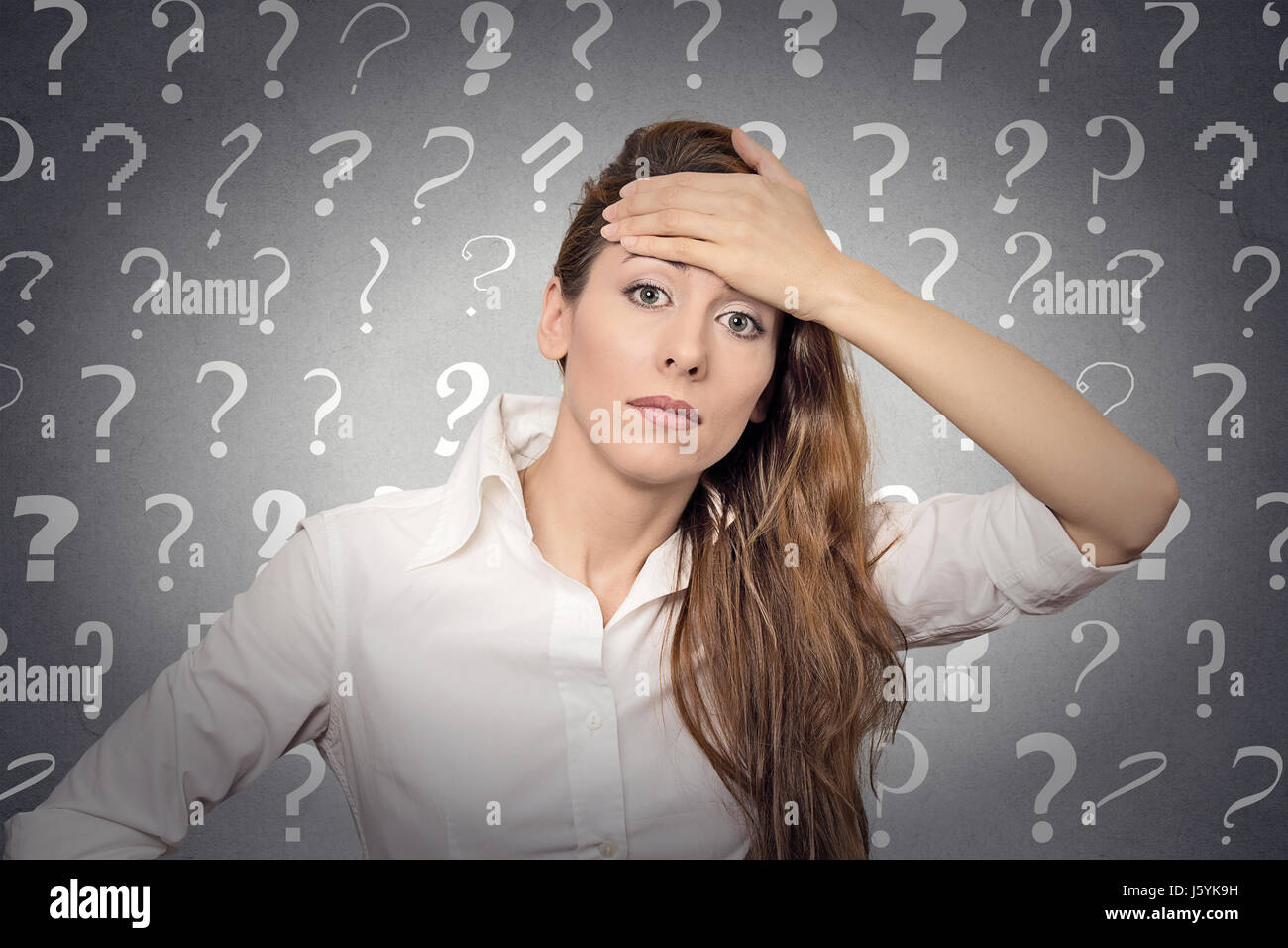 Portrait stressed woman with headache has many questions isolated grey wall background with question marks. Human emotion face expression feeling body Stock Photo