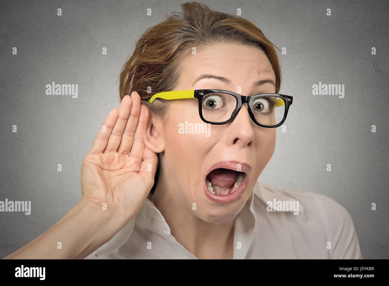 Closeup portrait young nosy woman hand to ear gesture trying carefully intently secretly listen in on juicy gossip conversation news privacy violation Stock Photo