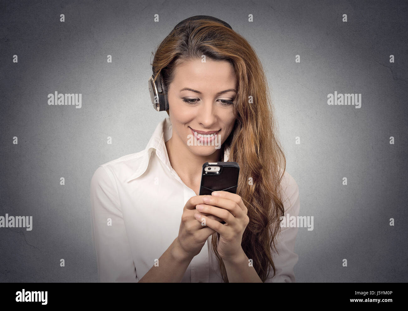 Closeup portrait happy looking, surprised businesswoman with headphones reading news, sms on smart phone holding mobile listening radio podcast isolat Stock Photo