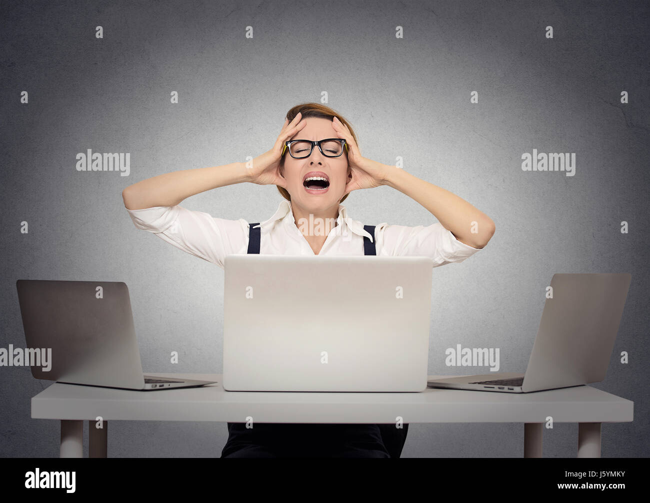 Stressed businesswoman sitting at table in front of multiple computers in her office having nervous breakdown. Negative human face expressions, emotio Stock Photo