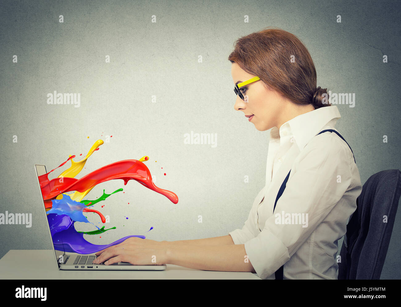 Side view profile attractive happy young business woman working on laptop computer colorful splashes coming out of screen liquid effect isolated grey  Stock Photo