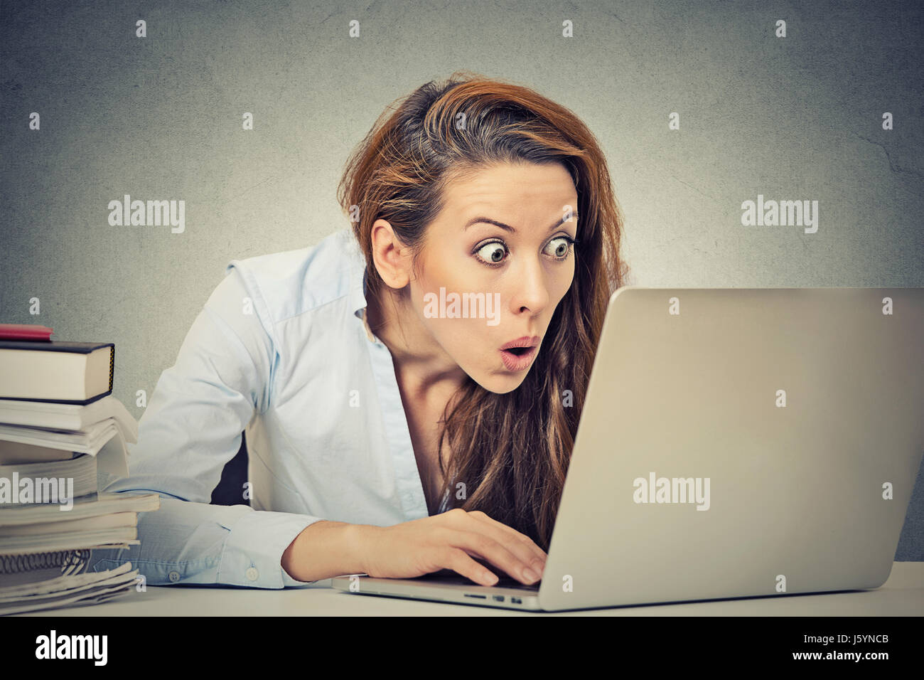 Portrait young shocked business woman sitting in front of laptop computer looking at screen isolated grey wall background. Funny face expression emoti Stock Photo