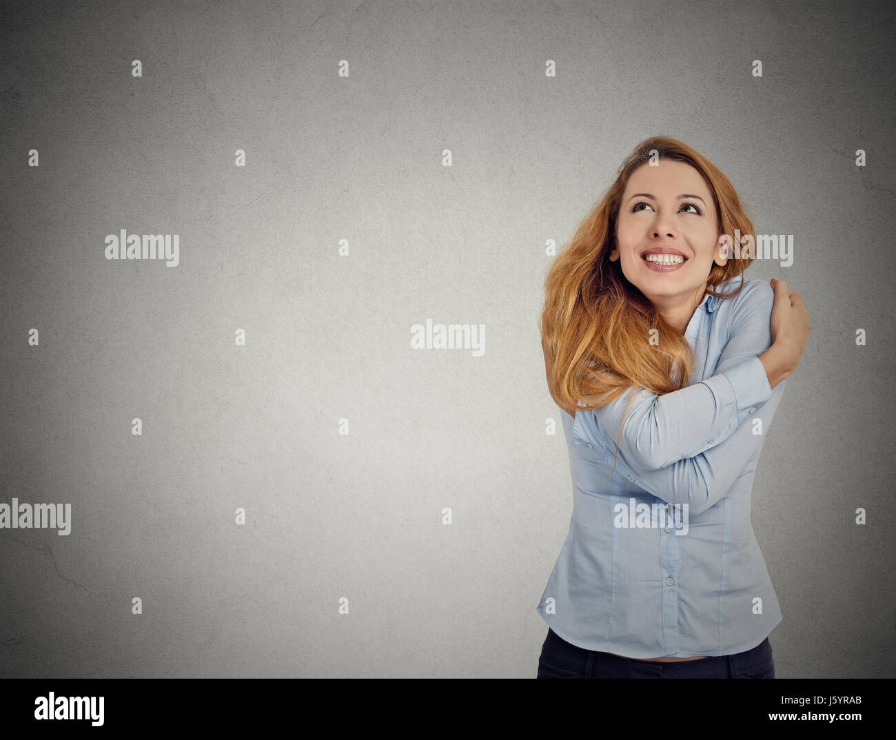 Closeup portrait confident woman holding hugging herself looking up at copy space isolated grey wall background. Positive emotion facial expression fe Stock Photo