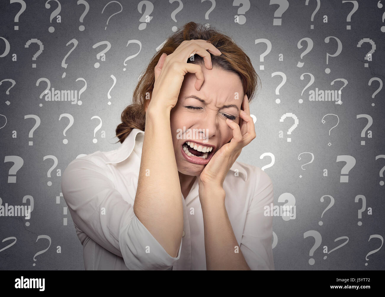 Portrait stressed crying woman has many questions isolated grey wall background with question marks. Human emotion face expression feeling body langua Stock Photo