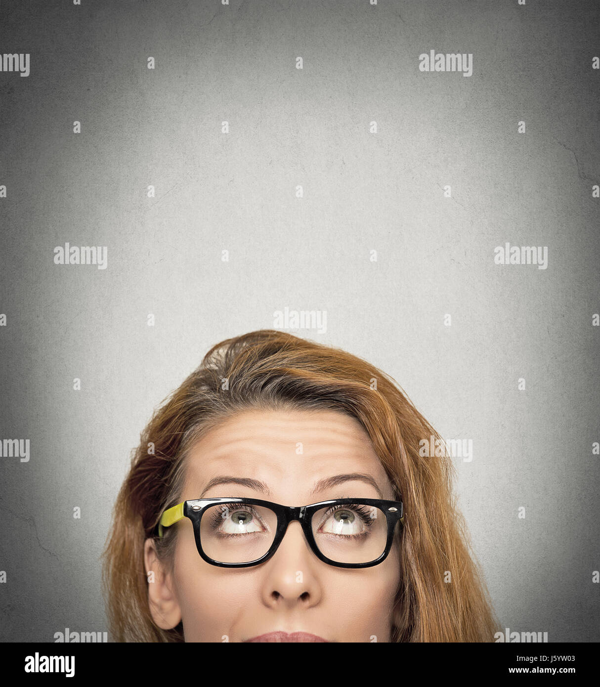 closeup portrait headshot woman looking up grey wall background with copy space above head. Human face expressions, emotions, feelings, body language Stock Photo