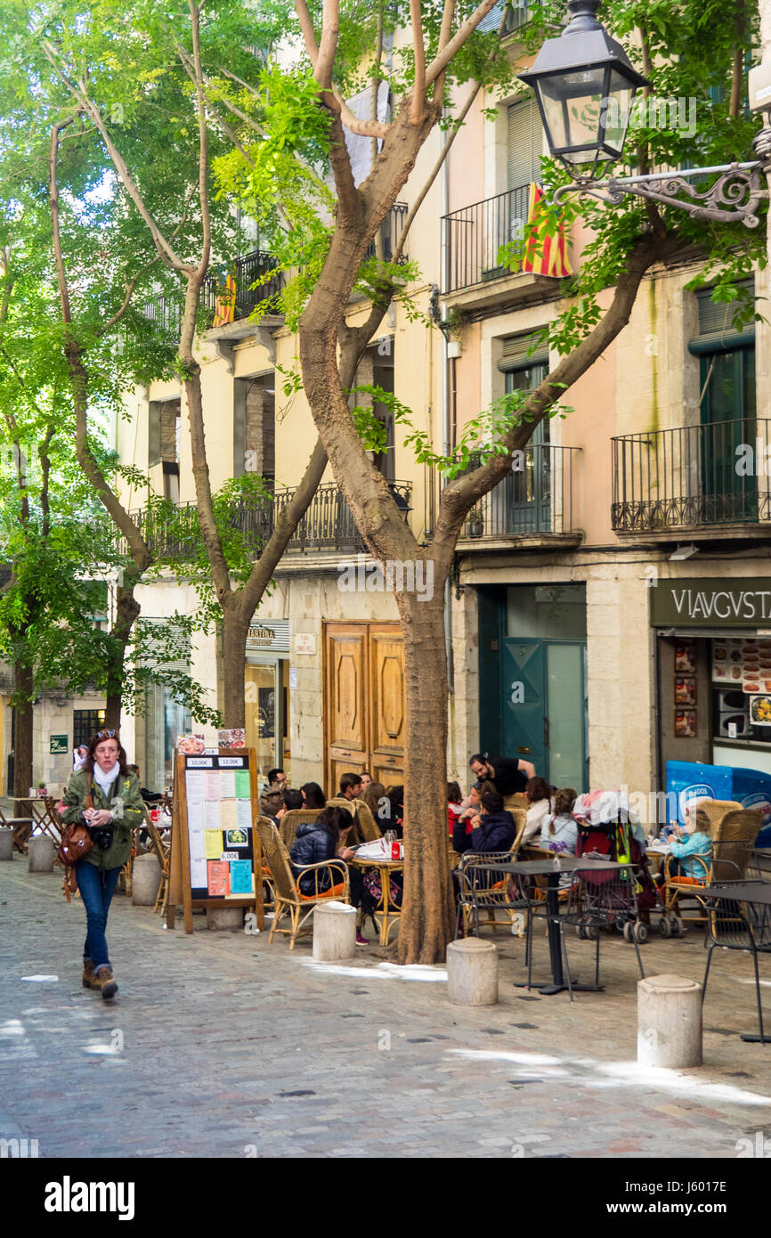 A woman walking along a street where diners are eating al fresco style in the old quarter of Girona, Spain. Stock Photo