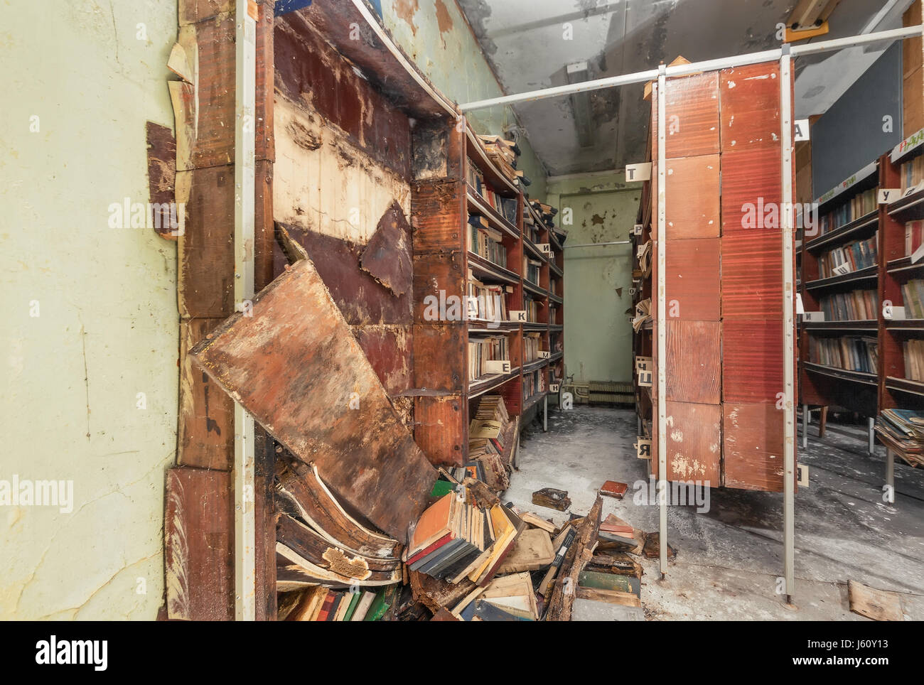 Bookcase with fallen off shelves and rotten books in an abandoned library Stock Photo
