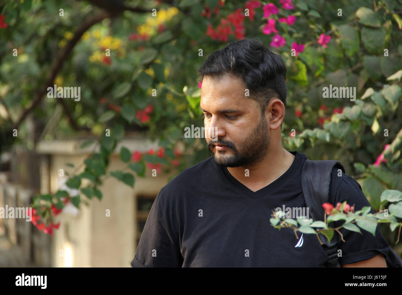 Young Indian man thinking looking down, with flowers in backdrop Stock Photo