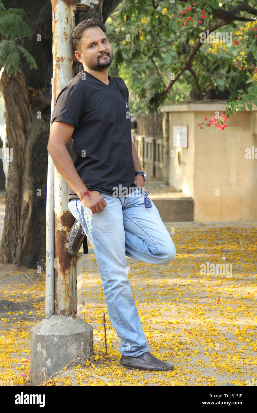 Young Indian man resting against light pole on a road side Stock Photo