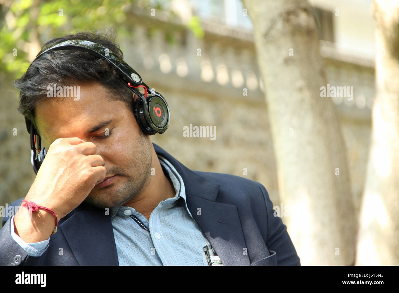 Young Indian corporate man listening to music closing his eyes in park Stock Photo