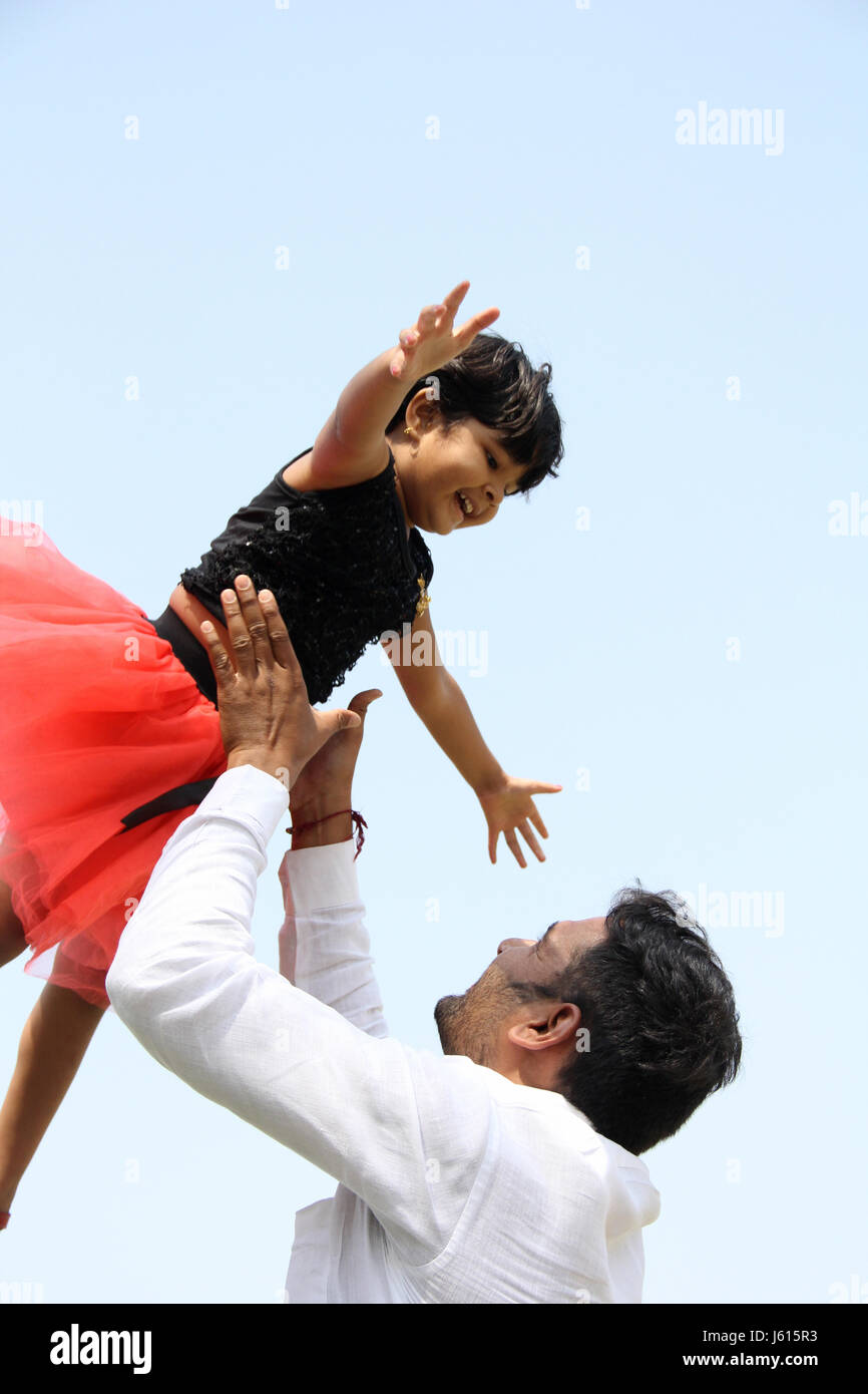 Young Indian father playing with his girl by throwing, tossing her high in the air Stock Photo
