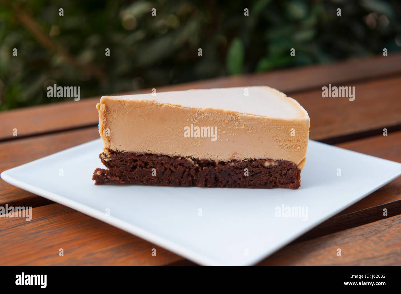 Slice of dulce de leche and chocolate brownie ice cream cake on a white plate outdoors Stock Photo