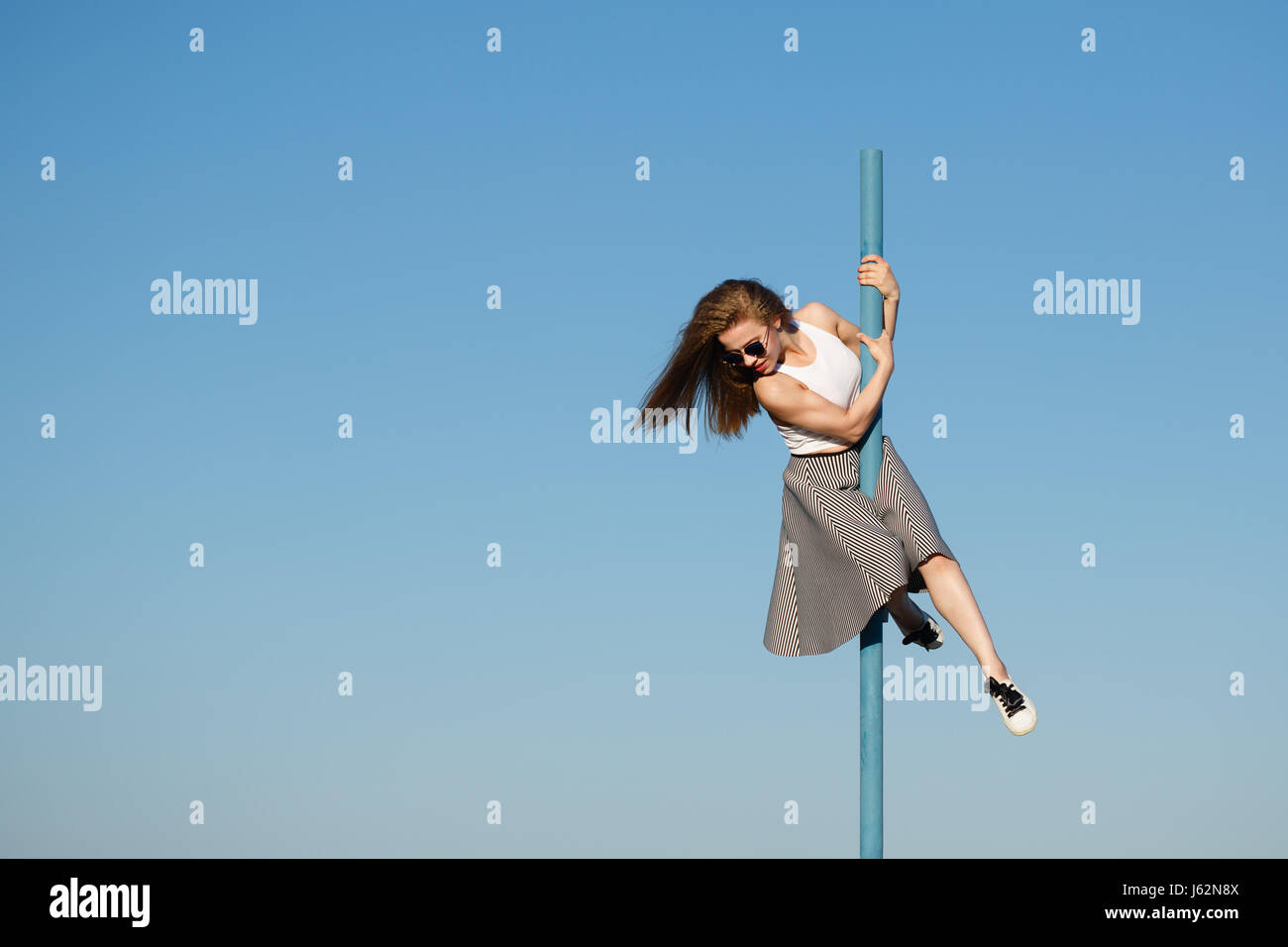 Young attractive girl hipster dancing on the pole. She is wearing a top, a skirt and sunglasses. Flying hair. The concept of life in motion. Stock Photo