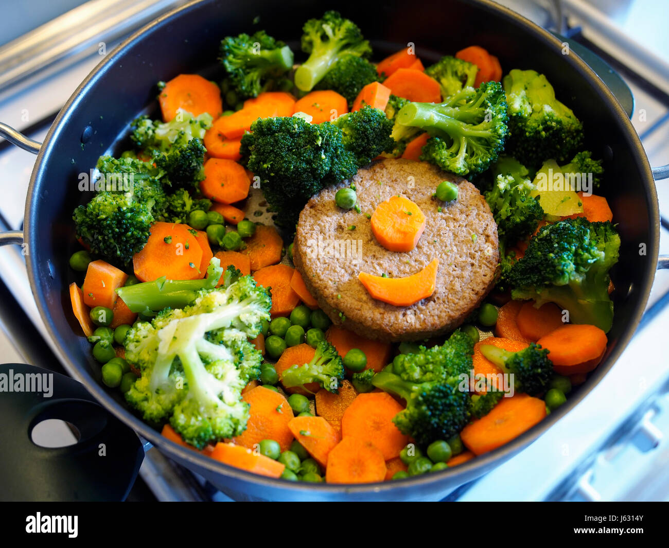 Vegan food: cooking a smiling soy burger and vegetables. Stock Photo