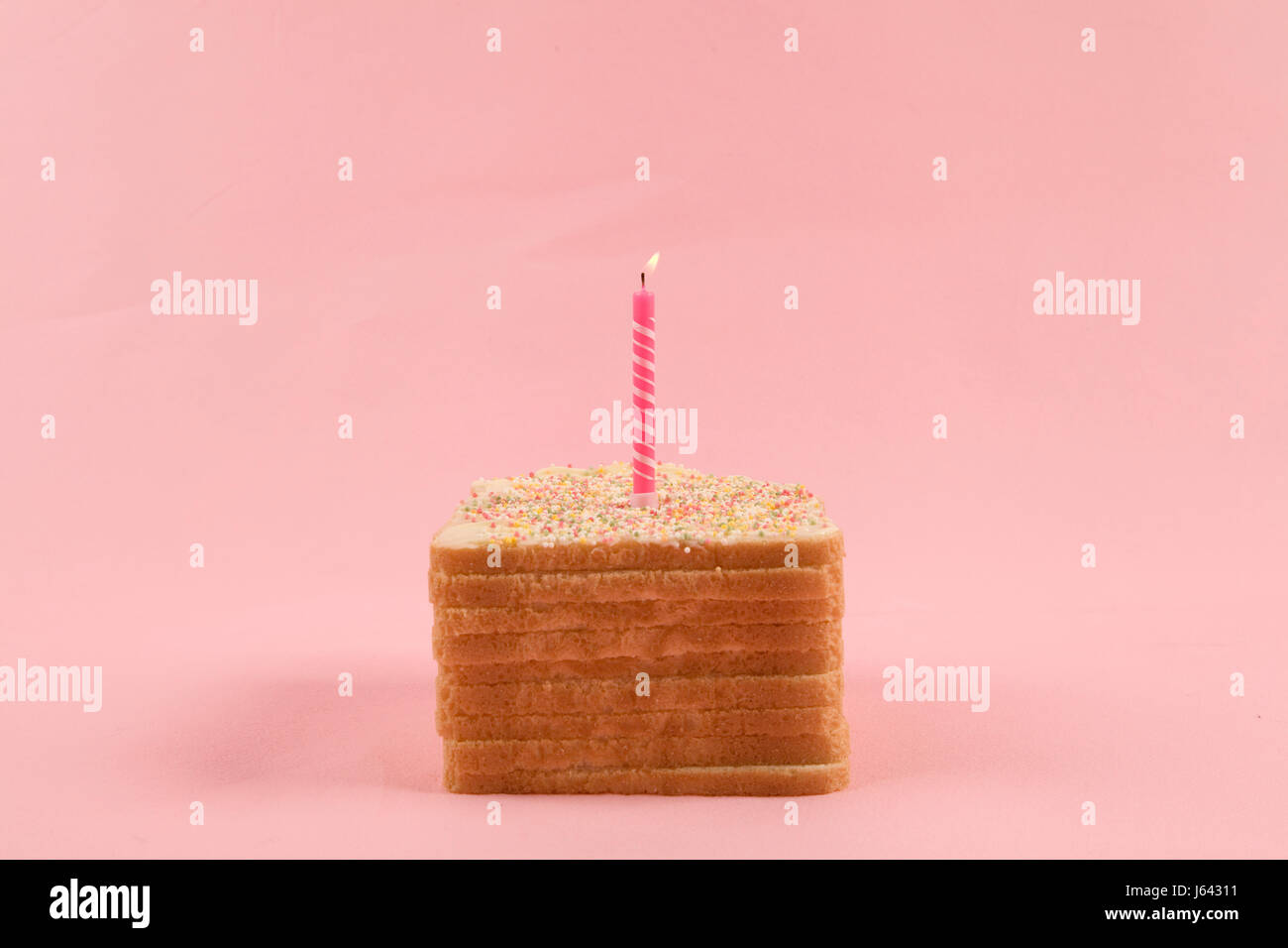 a quirky icing birthday bread covered with sprinkles on pink background Stock Photo