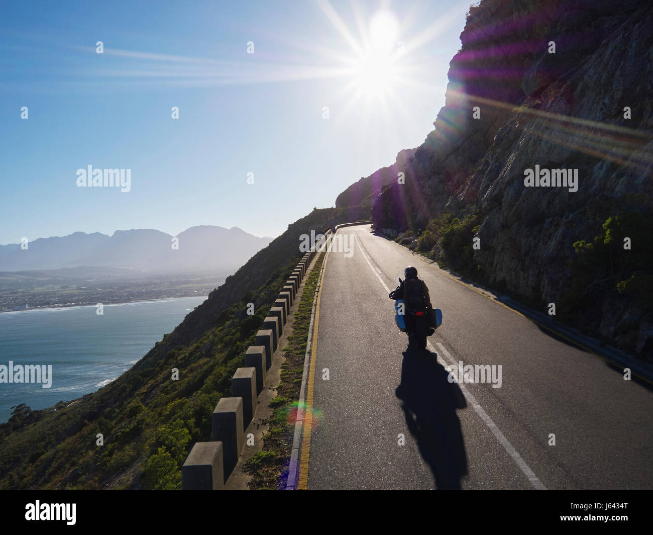 Couple riding motorcycle on sunny road along ocean Stock Photo
