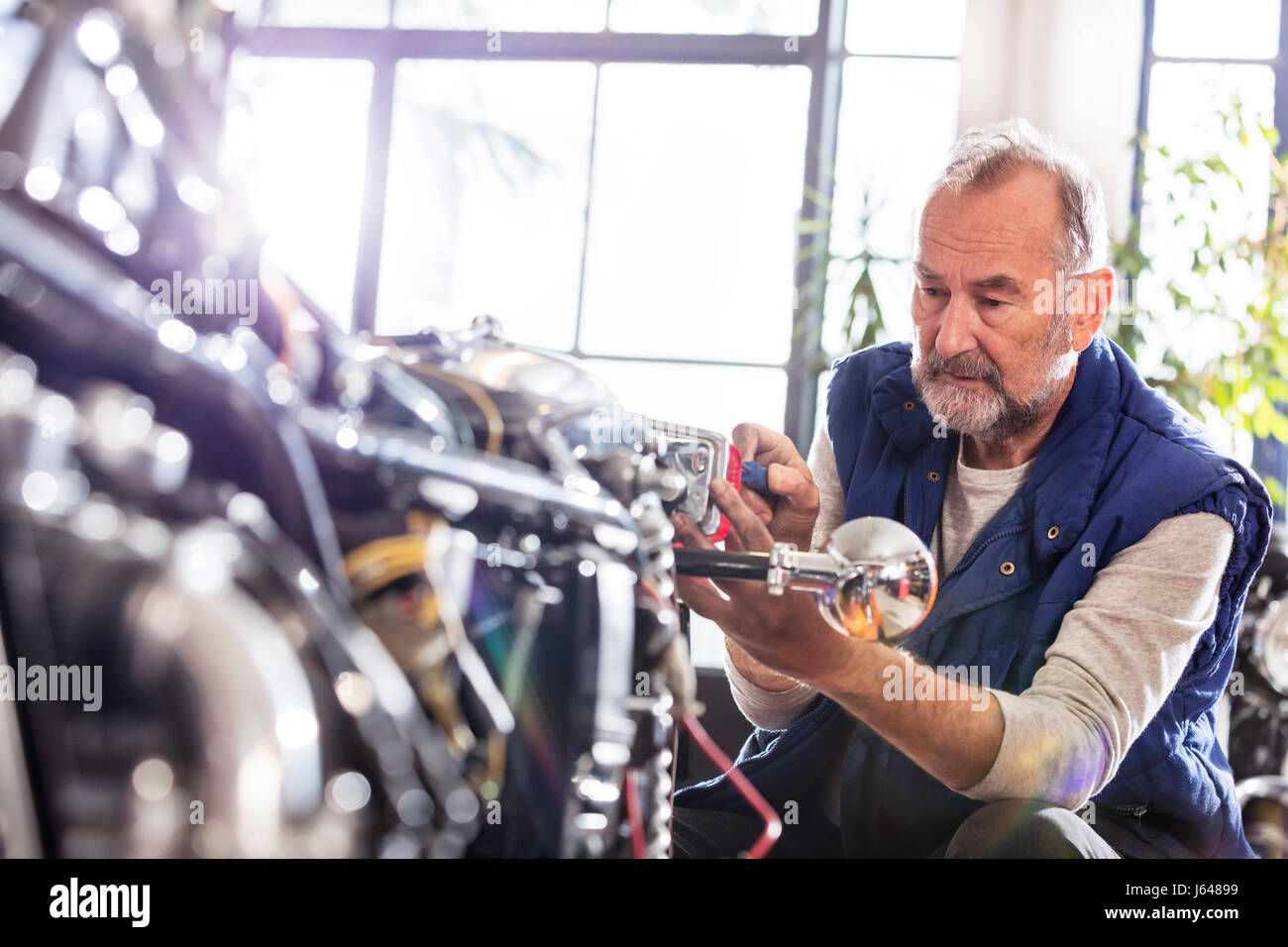 Senior male motorcycle mechanic fixing motorcycle in workshop Stock Photo