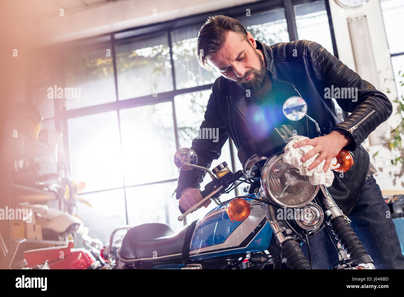 Male motorcycle mechanic wiping motorcycle in workshop Stock Photo