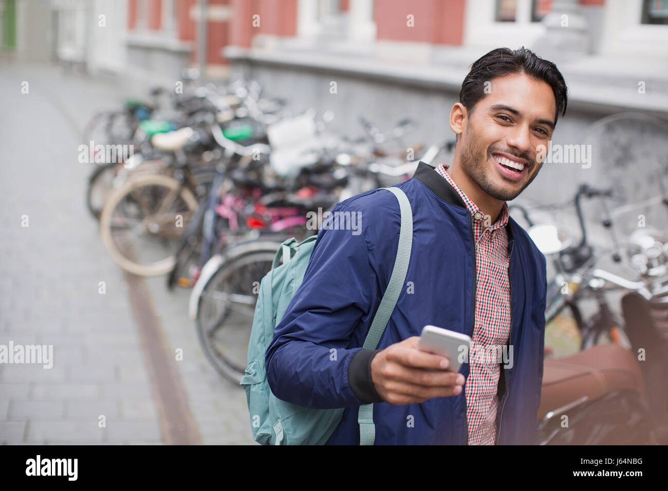 Portrait enthusiastic young man with cell phone at bike rack on city street Stock Photo