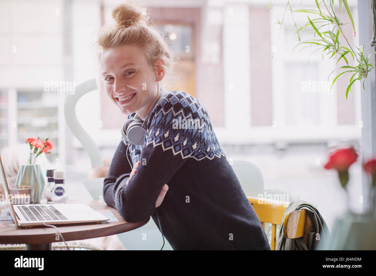 Portrait smiling young woman with headphones at laptop in cafe window Stock Photo