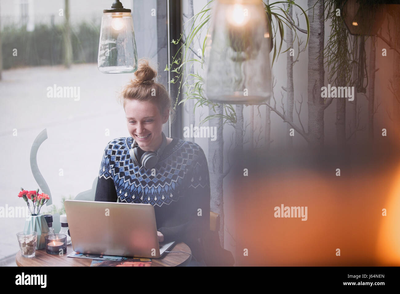 Smiling young woman using laptop in cafe window Stock Photo