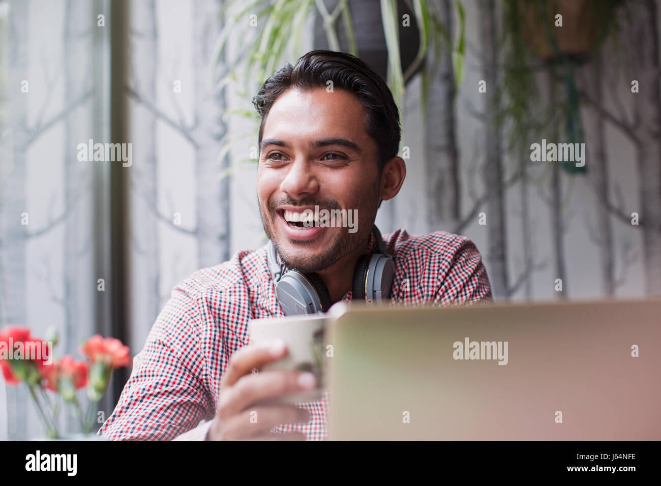 Man laughing and drinking coffee at laptop in cafe Stock Photo