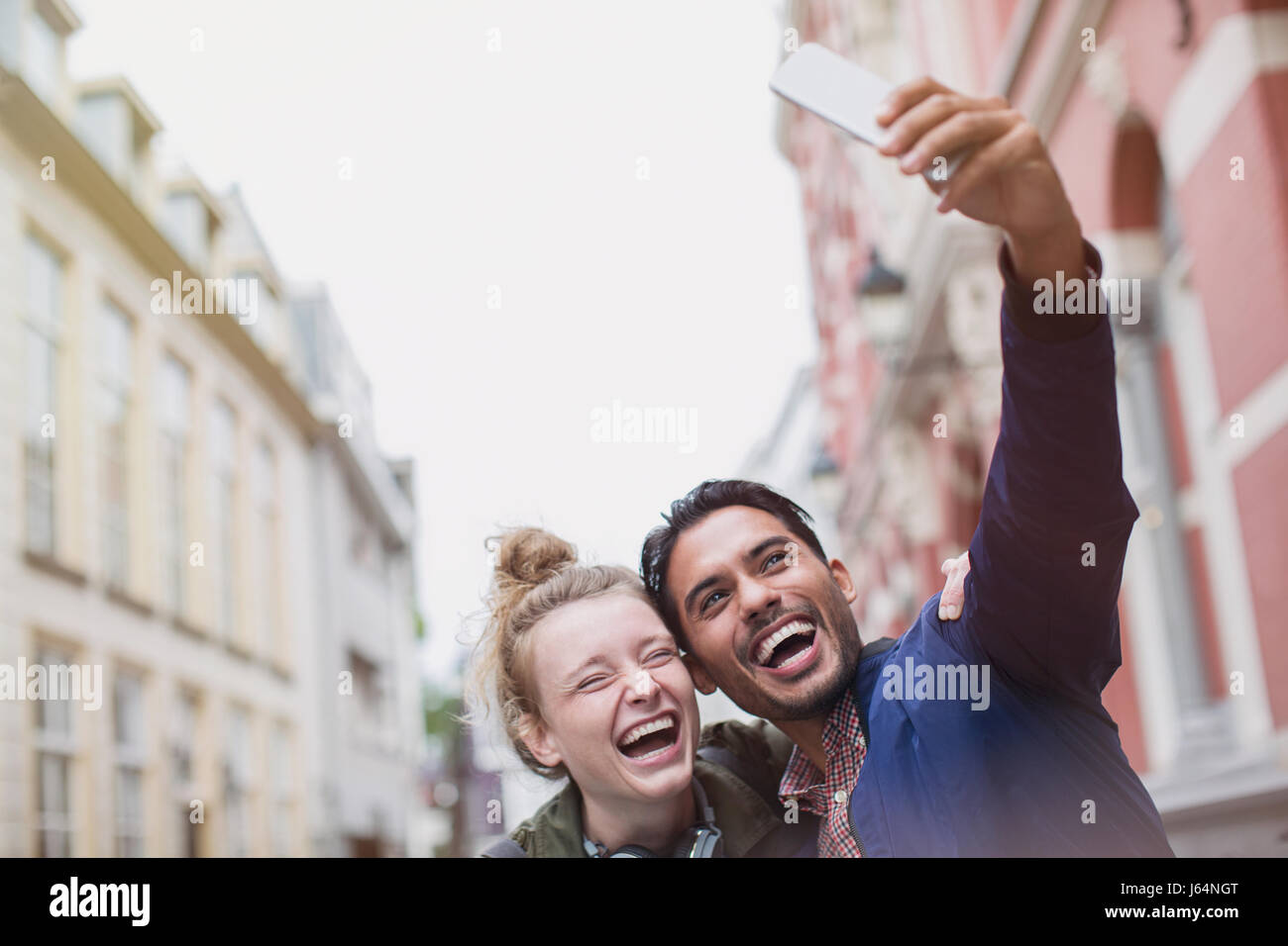 Enthusiastic, laughing young couple taking selfie in city Stock Photo