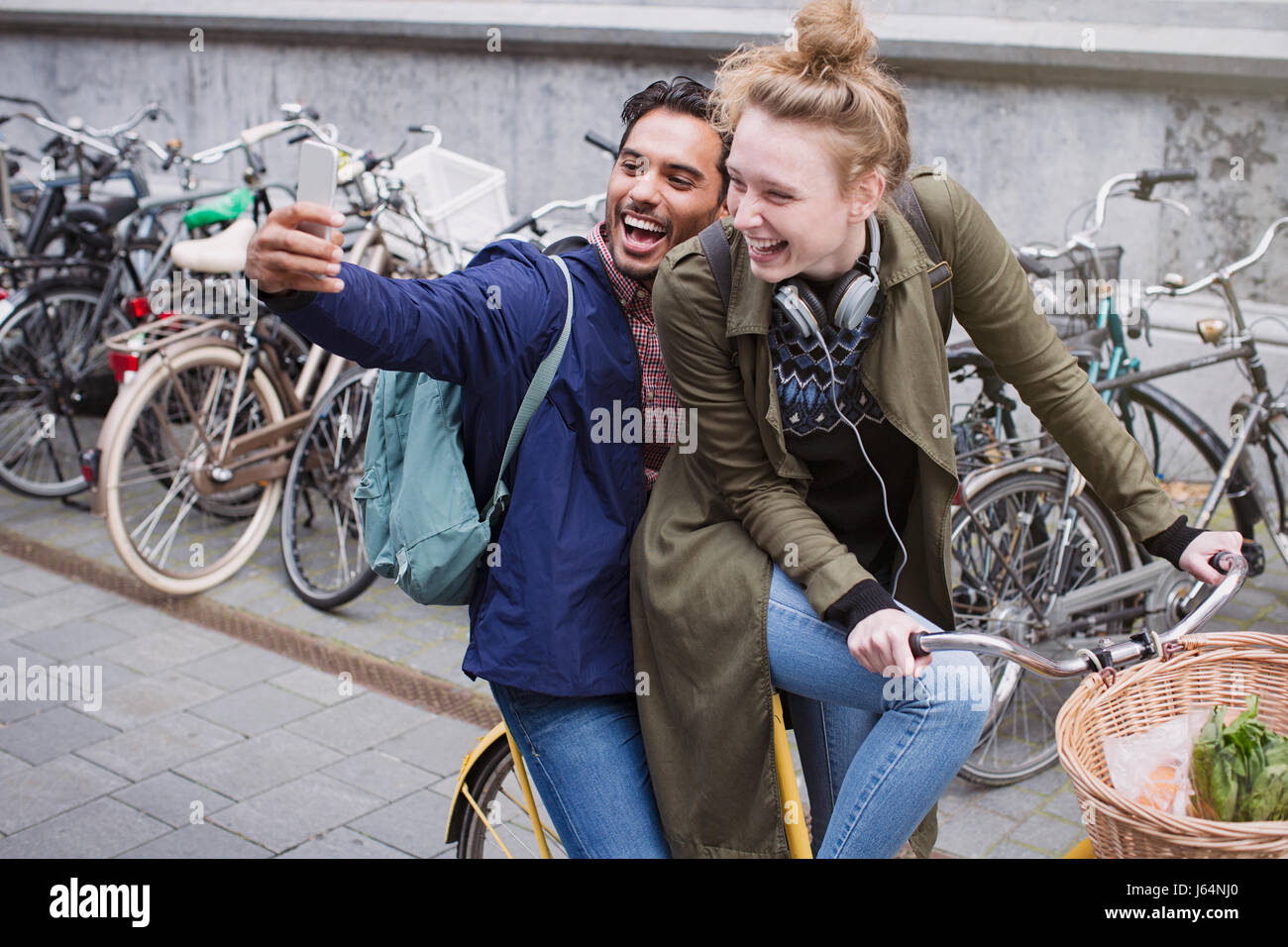 Playful, laughing young couple taking selfie with camera phone on bicycle Stock Photo