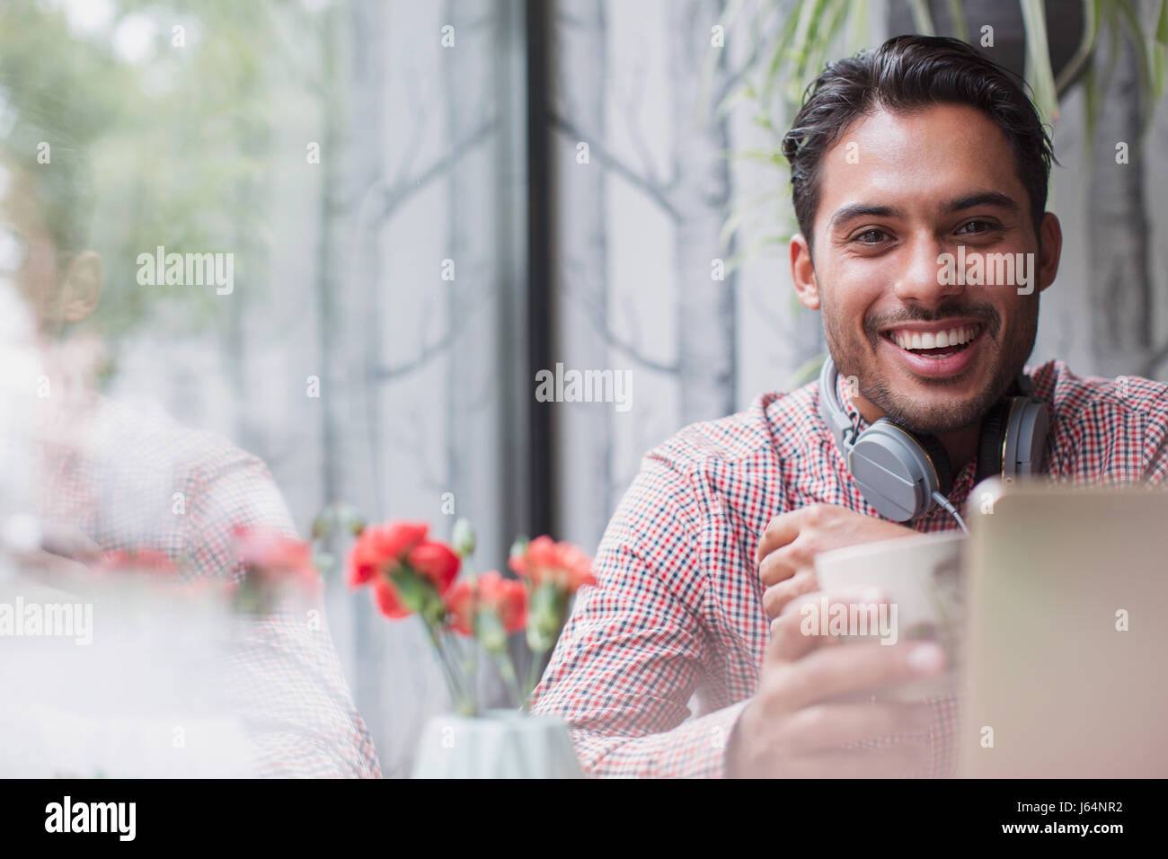 Portrait smiling young man with headphones drinking coffee at laptop in cafe window Stock Photo