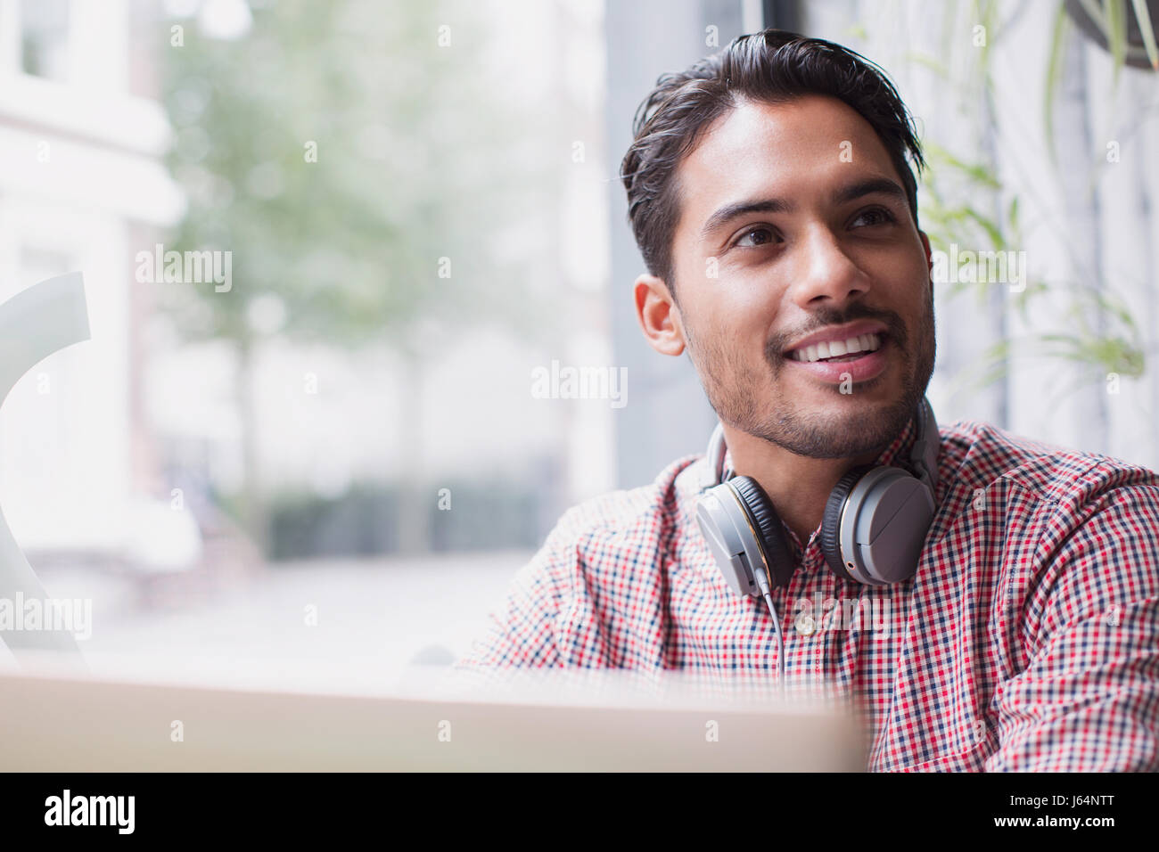 Smiling young man with headphones at laptop in cafe window Stock Photo