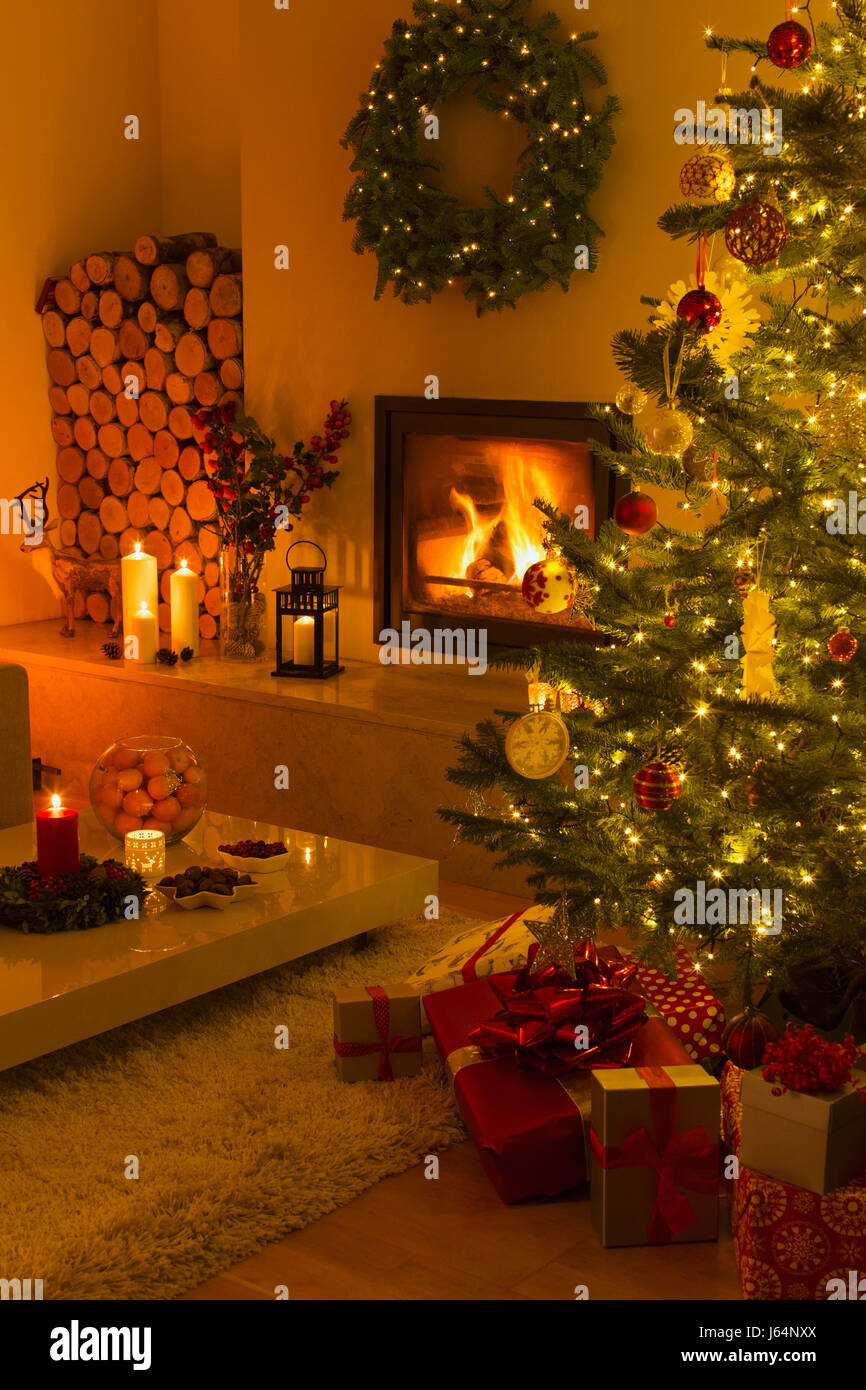 Ambient fireplace and candles illuminating living room with Christmas tree and decorations Stock Photo