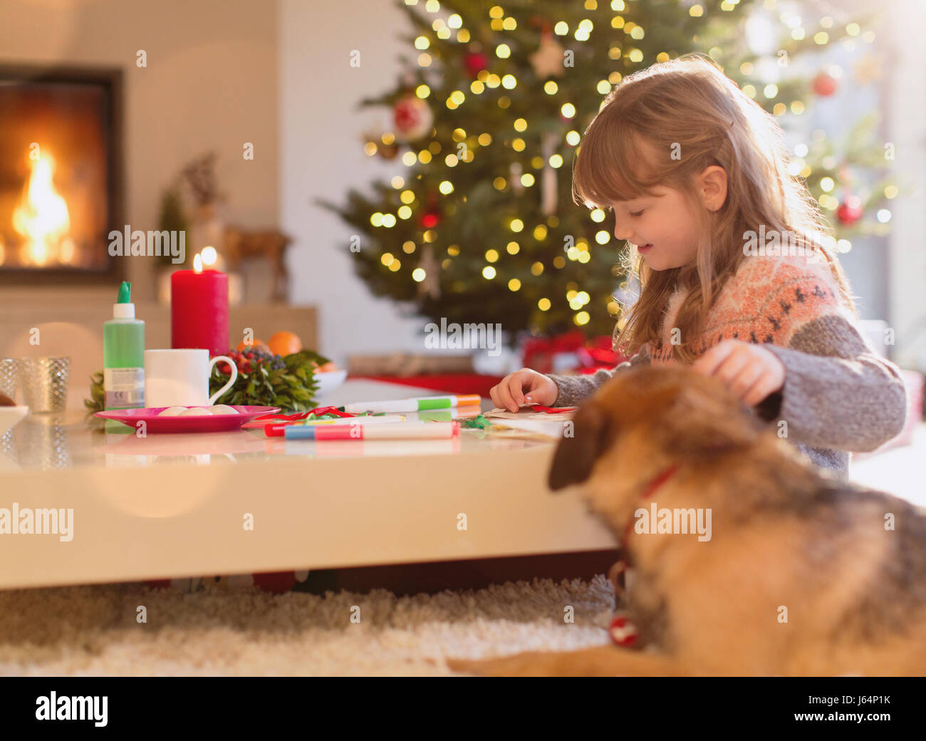 Dog watching girl coloring with markers in Christmas living room Stock Photo