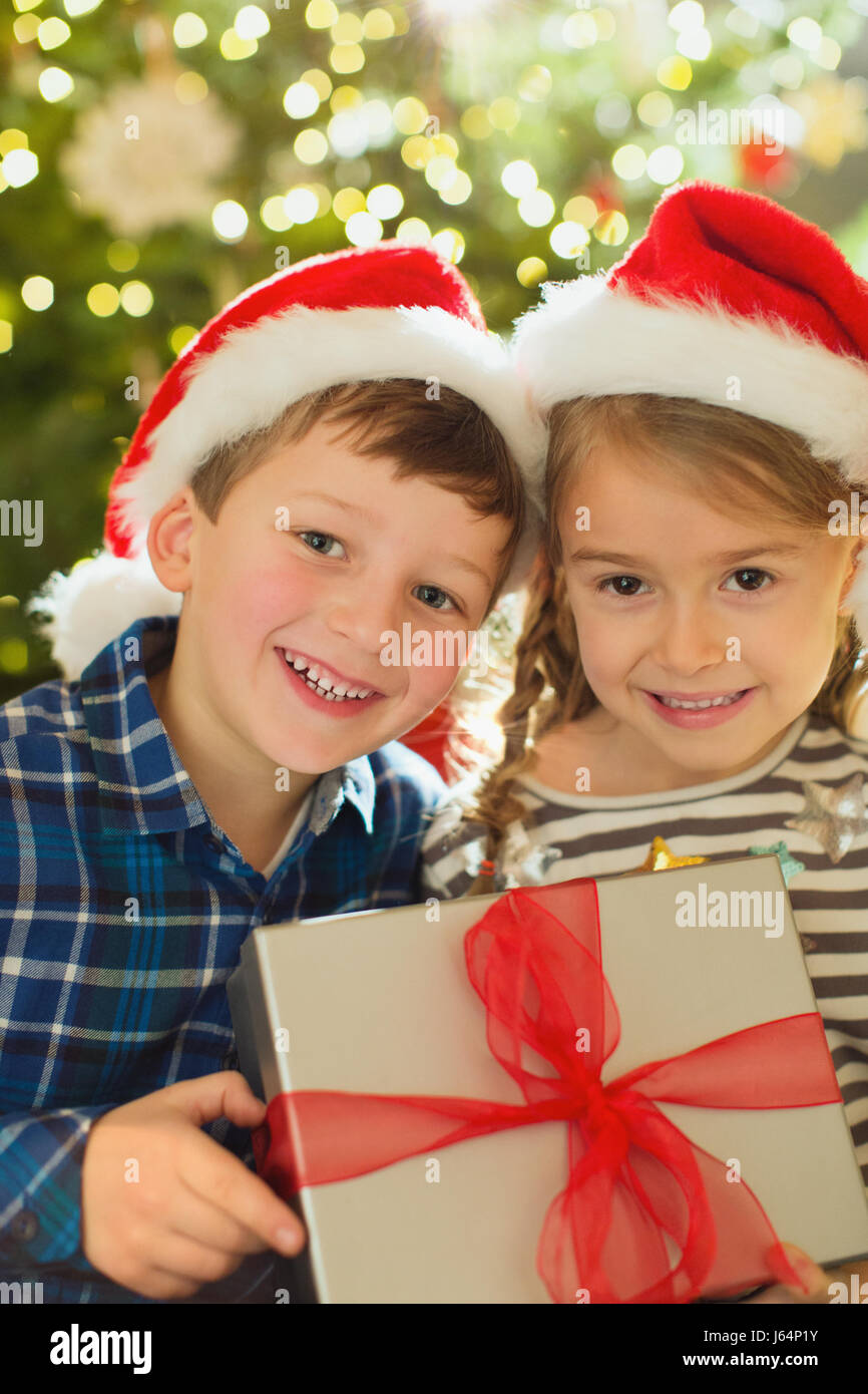 Portrait smiling brother and sister in Santa hats holding Christmas gift Stock Photo