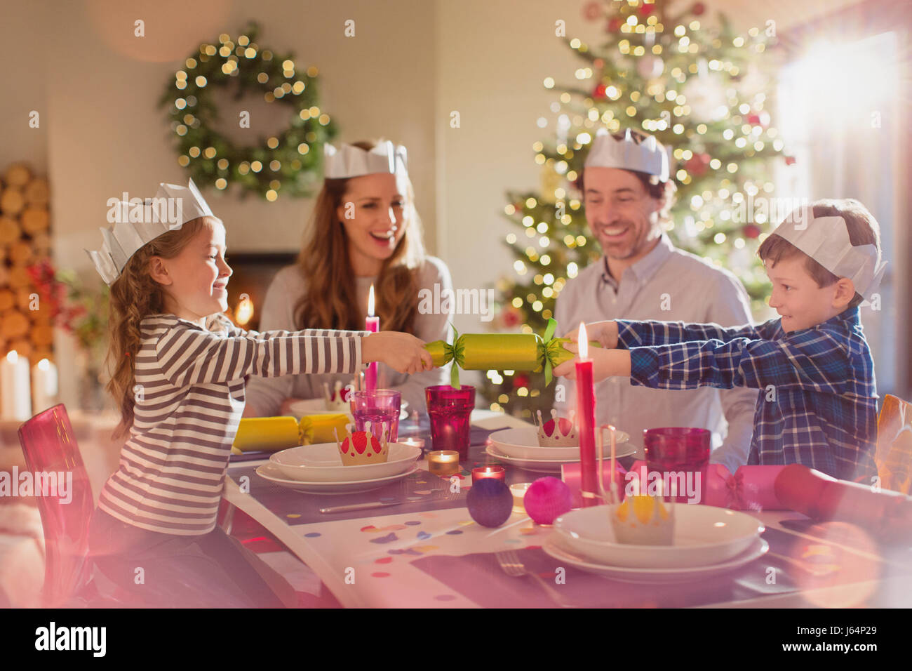 Family in paper crowns pulling Christmas cracker at dining table Stock Photo