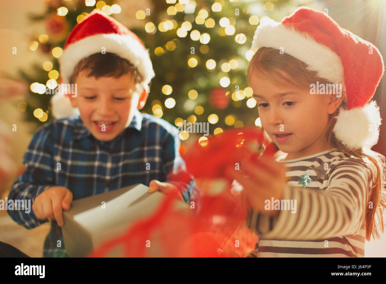 Brother and sister in Santa hats opening Christmas gift Stock Photo