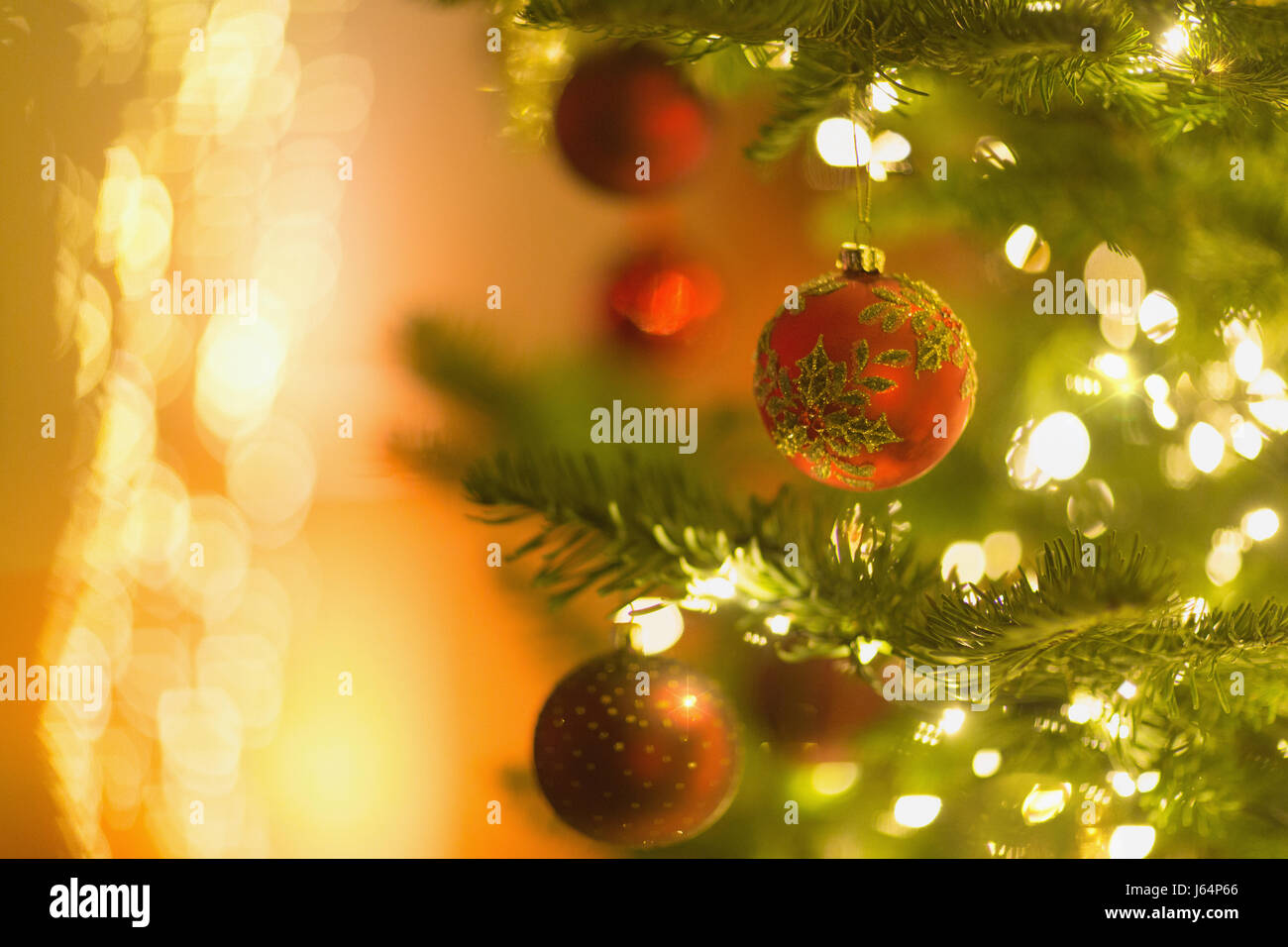 Red ornaments hanging from branch of Christmas tree with string lights ...