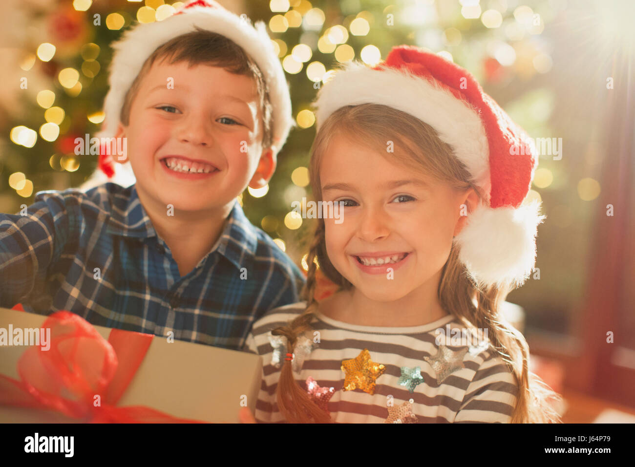 Portrait smiling, enthusiastic brother and sister wearing Santa hats holding Christmas gift Stock Photo