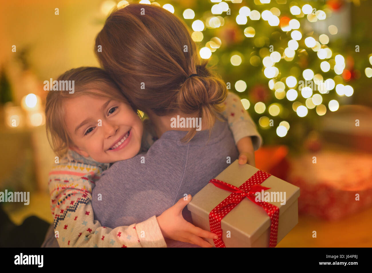 Smiling daughter with Christmas gift hugging mother Stock Photo