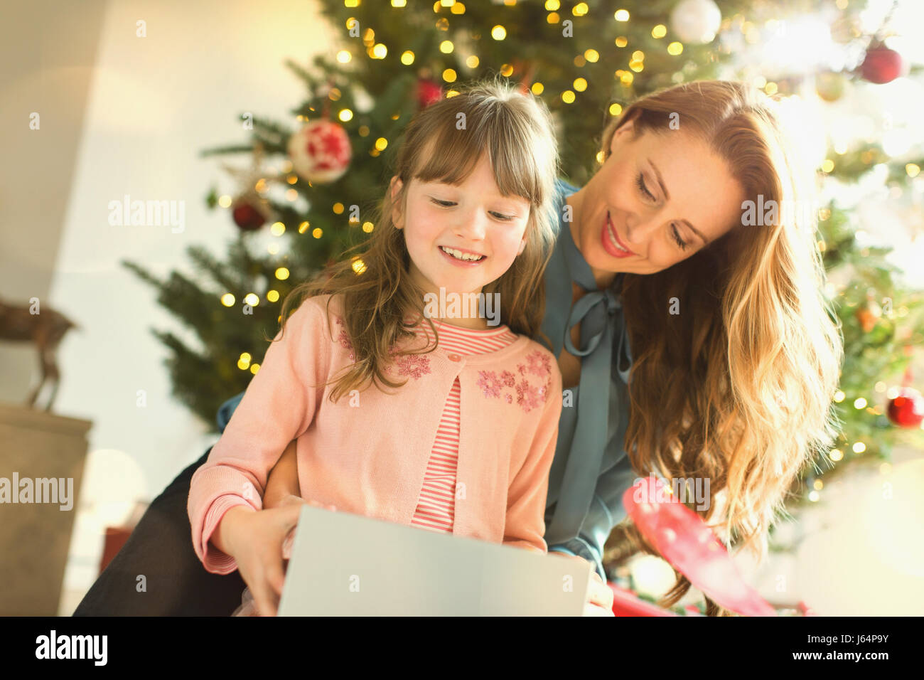 Mother watching daughter opening Christmas gift Stock Photo