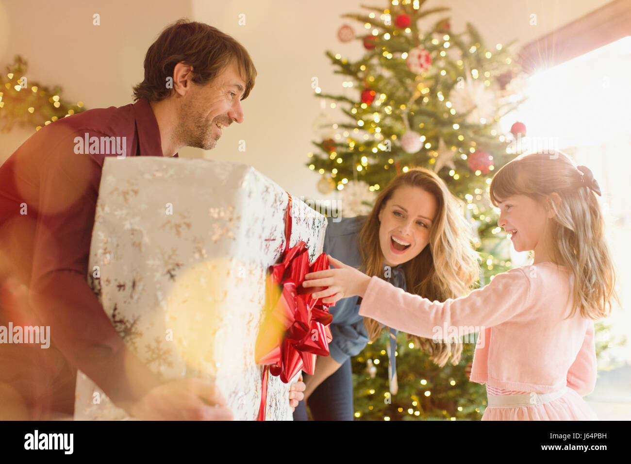 Parents giving large Christmas gift to daughter near Christmas tree Stock Photo